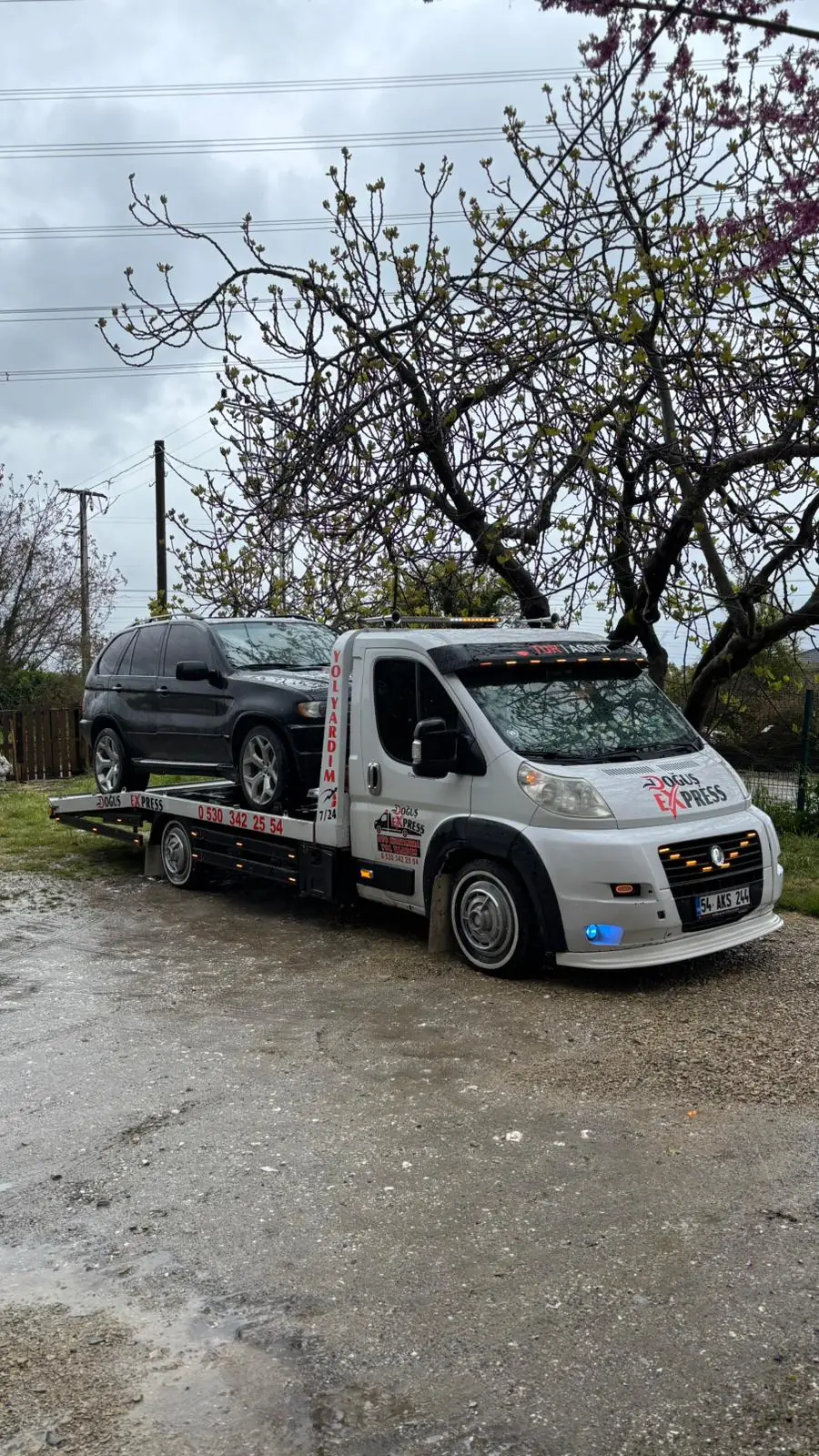 Yağmur sonrası kırsal yolda araç taşıyan platformlu çekici