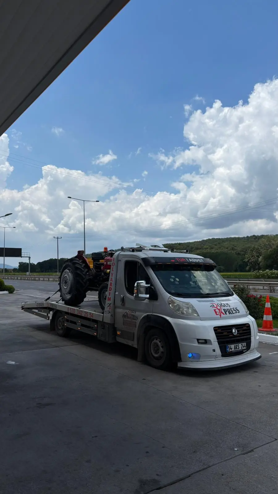 Kırmızı traktörün çekici platformuna yüklenmiş hâlde taşınması